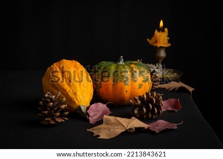 Close-up of still life with pumpkins, autumn leaves and lit candle, selective focus, on tablecloth and black background, horizontal, with copy space