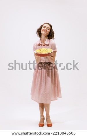 Portrait of beautiful woman holding apple pie isolated over white background. Wife duties. Cooking activity. Concept of beauty, retro style, fashion, elegance, 60s, 70s, family. Copy space for ad Royalty-Free Stock Photo #2213845505