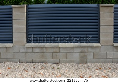 metal fillings of the fence with an underlay of concrete blocks. A metal aluminum fence will provide privacy around the garden. horizontal slats cover well. a hedge made of tuji adds protection Royalty-Free Stock Photo #2213854475