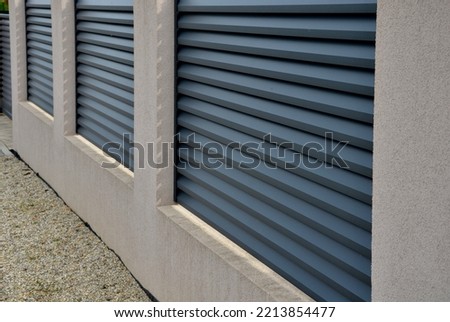 metal fillings of the fence with an underlay of concrete blocks. A metal aluminum fence will provide privacy around the garden. horizontal slats cover well. a hedge made of tuji adds protection Royalty-Free Stock Photo #2213854477