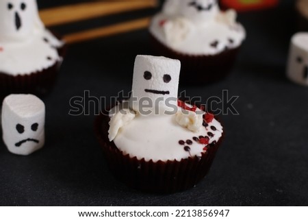 delicious chocolate cupcakes with white cream and marshmallows painted with funny faces on a dark background selective focus, halloween theme
