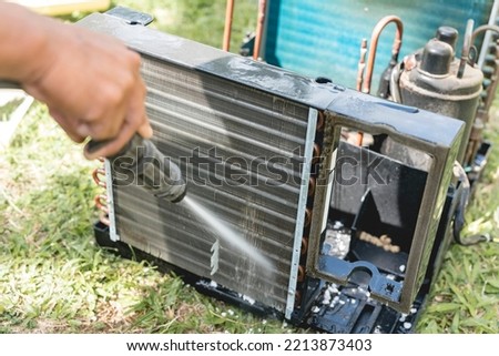 A man washes and cleans the evaporator coil of an old window type air conditioning unit with a high pressure hose Royalty-Free Stock Photo #2213873403