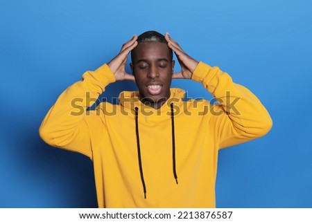 Young African American man pictured isolated on blue background with hands on head