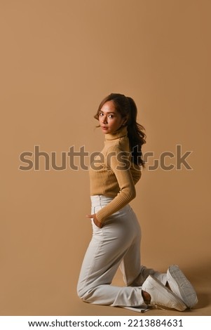 Attractive fashionable woman posing on beige background. Fashion studio photo, Autumn and Winter concept