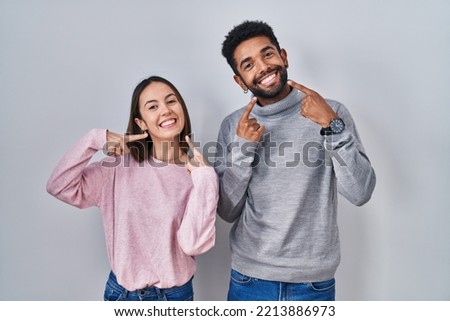 Young hispanic couple standing together smiling cheerful showing and pointing with fingers teeth and mouth. dental health concept. 