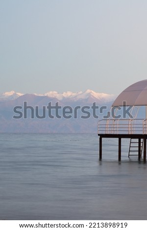 Sunset view from north shore of the Lake Issyk-Kul on pier and high snow covered mountain peaks Tien Shan on south shore, Kyrgyzstan