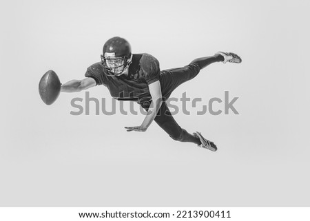 Dynamic portrait of young man, american football player catching ball. Black and white photography. Full equipment. Concept of sport, retro style, 20s, fashion, action, college sport, youth