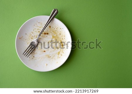 White ceramic plate with food leftover, pasta, olive oil, sauce and fork on green background. Creativity picture with space for text 