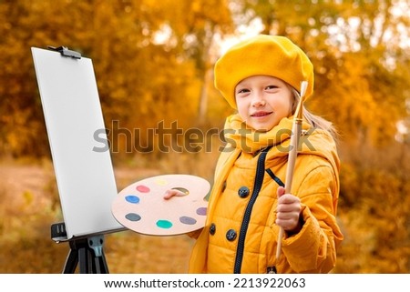 Autumn Baby Girl Drawing in Fall Leaves Park, Little Kid Painting, Children Creativity. little girl artist with a brush and paints in her hands in autumn in the park draws a landscape with leaves 
