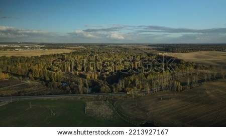 Agricultural fields. On the horizon you can see the settlement and the highway. Around the forest with colorful autumn leaves. Aerial photography.
