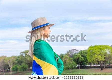 Woman wrapped in a brazilian flag wearing hat and jeans. Agribusiness woman. Royalty-Free Stock Photo #2213930395