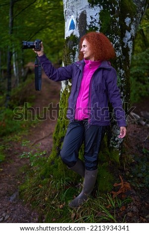 Redhead woman with curly hair and camera hiking on a trail in the mountain forest