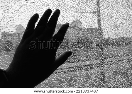 Black and white photo of a hand put on cracked window.