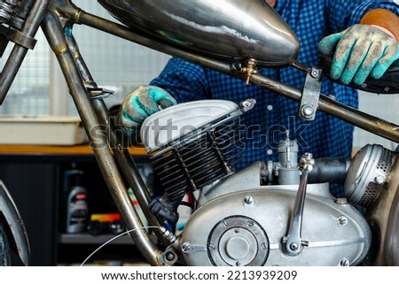 Bike maintenance and repair. Mechanic man fixing motorbike in garage.  Biker man woking on fixing repairing old classic motorcycle's engine for a new season, basic motorcycle maintenance for hobby. 