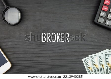 BROKER - word (text) and money dollars on the table, phone magnifying glass (loupe) and calculator. Business concept, buying goods and products, paying for services (copy space).