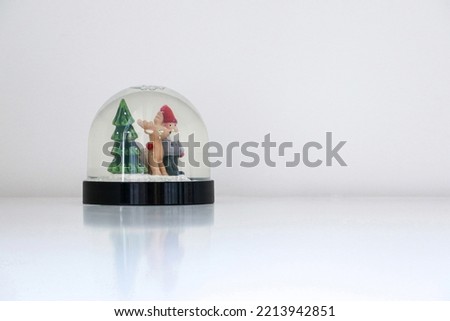 Christmas snow globe, with Santa Claus, his reindeer and a Christmas tree, on white snowy background, staring at copy space on the right