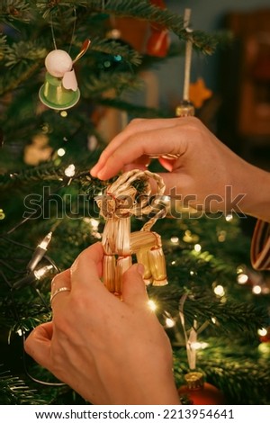 Close up of woman hand decorating christmas tree with straw reindeer figure