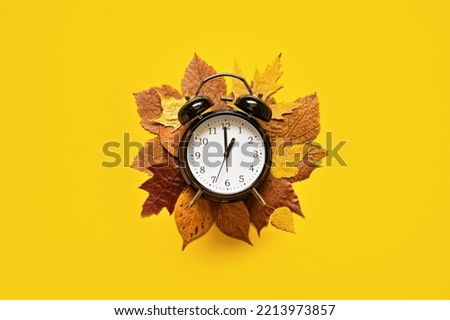 Daylight saving day. Fall Back. Black Alarm clock and autumn leaves on yellow background. Daylight saving time end Royalty-Free Stock Photo #2213973857