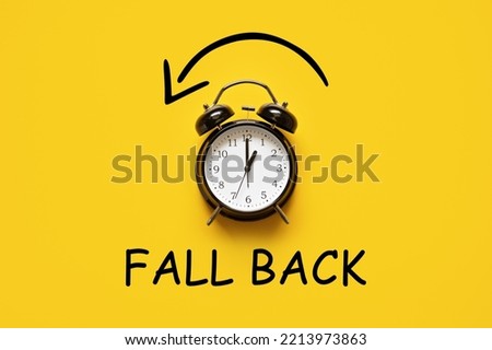 Daylight saving day. Fall Back. Black Alarm clock and autumn leaves and text Fall Back on yellow background. Daylight saving time end Royalty-Free Stock Photo #2213973863