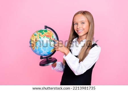 Portrait photo of little preteen child schoolgirl wear uniform blonde hair hold globe finger point map geography lesson isolated on pink color background