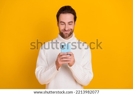 Photo of positive cheerful guy dressed white sweater typing modern device isolated yellow color background