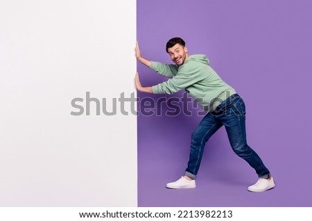 Full body photo of attractive young man pushing white banner wall cheerful wear trendy gray outfit isolated on violet color background