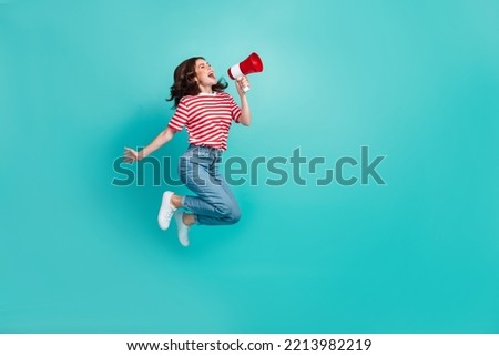 Full length photo of pretty cute girl dressed red t-shirt jumping high shouting bullhorn empty space isolated teal color background