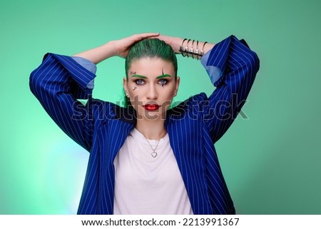 Woman with creative joker makeup. Trendy halloween carnival costume. Green background blue jacket. Stylish fantasy glamorous make-up.   image expression masquerade party. All Saints' Day	