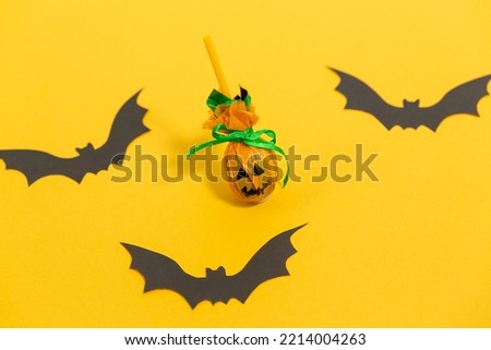 Step by step instruction of easy making Halloween decor - funny orange pumpkin with scary face from lollipop on yellow background with black bats. Step 2 - finished work. Creative DIY crafts for kids.