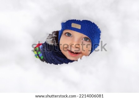 Boy looks through a hole in the wall of a snow castle. Boy plays with snow