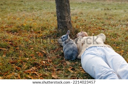 Adorable young rabbit and woman sit together outdoor in autumn forest. Asian woman wear warm sweater with pet in relax and calm.