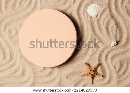 Empty beige round platform podium for cosmetics or products presentation, sea shell and starfish on natural beige beach sand background. Wavy curved ornaments on sand, drawn by hand. Top view
