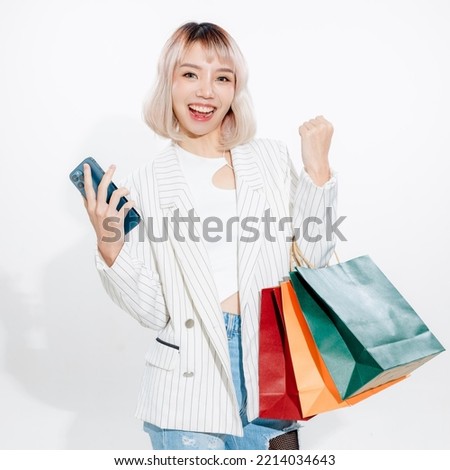 Young energetic Asian woman holding blank use smartphone searching shop retail with colorful shopping bags on white background. Online shoping futuristic concept. Royalty-Free Stock Photo #2214034643