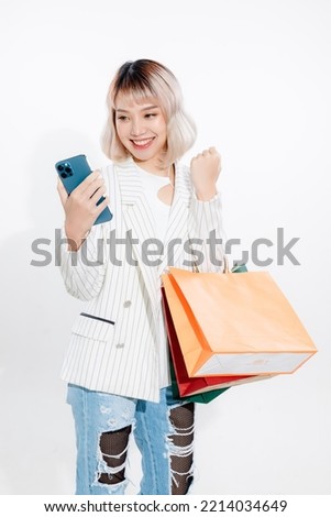 Young energetic Asian woman holding blank use smartphone searching shop retail with colorful shopping bags on white background. Online shoping futuristic concept. Royalty-Free Stock Photo #2214034649
