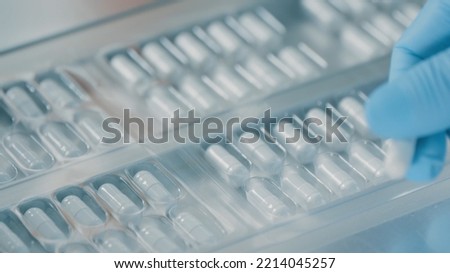 Pharmacologist checks blister packs with medicinal capsules moving on a conveyor. Plastic package with capsule meds. Medication capsules in blisters. Pharmaceutical factory production line. Macro Royalty-Free Stock Photo #2214045257