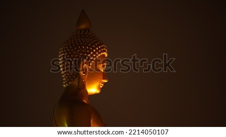 Golden big Buddha head and side of face on dark background. Lighting under chin. Big Buddha of Pak nam temple in Bangkok. Religion famous tourist place.