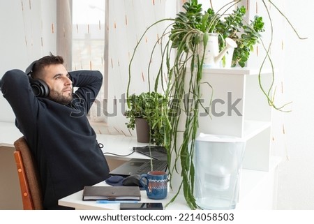 Bearded Caucasian man, Quiet quitting,  doing only what is expected or the bare minimum of job requirements. Man relaxing at work place with green potted plants. Royalty-Free Stock Photo #2214058503