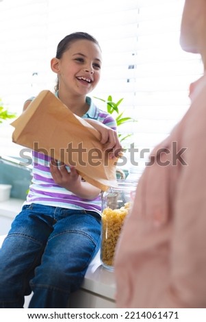 Vertical pictures of caucasian mother and daughter unpacking shopping bag together in the kitchen. Spending family time together at home.