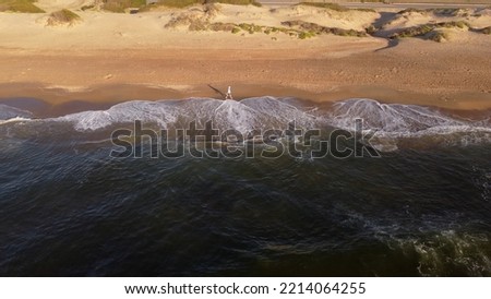 Man walking on beach at sunrise with city in background, Punta del Este in Uruguay. Aerial panoramic view. Royalty-Free Stock Photo #2214064255