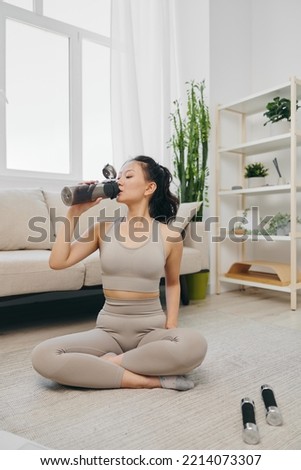 Sporty Asian woman in a yoga suit blogger watching a laptop recording of a sports workout online smiling and drinking water while relaxing at home, lifestyle in sports and good nutrition