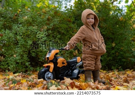a little boy stands next to a motorcycle on the street in autumn