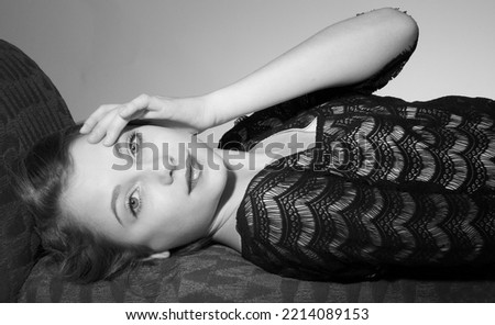 Black and white studio portrait of an elegant and attractive teen girl with short blonde hair lying on a sofa.