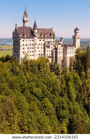Neuschwanstein Castle in forest, Germany. Vertical view of old German palace on mountain top, landmark of Bavaria in Munich vicinity. Theme of nature, travel, tourism, famous castle and king Ludwig.