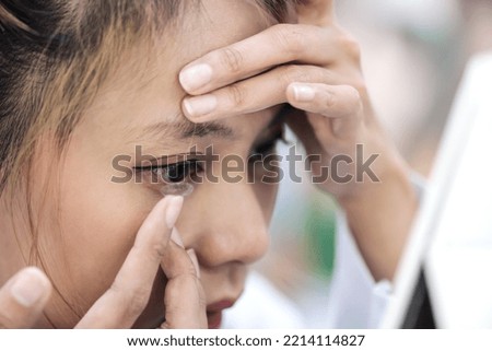 Close up woman hands holding contact len and putting in the eye at optical clinic, female wearing contact len and looking in the mirror in optic clinic, woman using contact lenses for eyesight vision Royalty-Free Stock Photo #2214114827