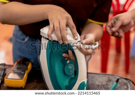 Close up hands of professional electrician man repairing electric iron in repair shop, repair man checking and fixing broken iron in electronic shop, household appliance maintenance service Royalty-Free Stock Photo #2214115465