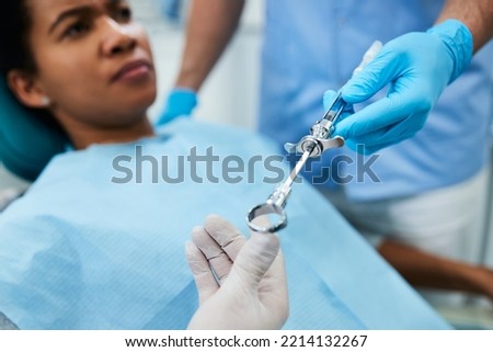 Close up of dental assistant passing syringe to a dentist during patient's dental procedure. Royalty-Free Stock Photo #2214132267