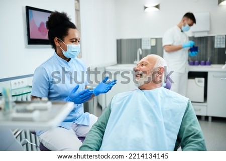 African American dental assistant communicating with senior patient during dental procedure at dentist's office. Royalty-Free Stock Photo #2214134145