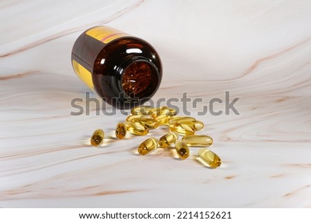 Capsules of fish oil spilled out open container on a marble counter.