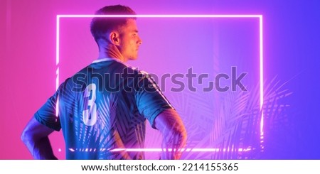 Rear view of caucasian male player wearing number 3 jersey over illuminated rectangle and plants. Pink, copy space, blue, composite, sport, soccer, competition, neon, glowing and abstract concept.