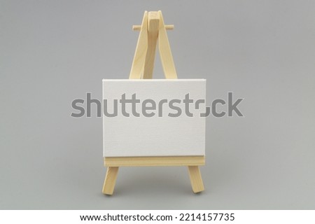 Wooden easel with white canvas on gray background. 